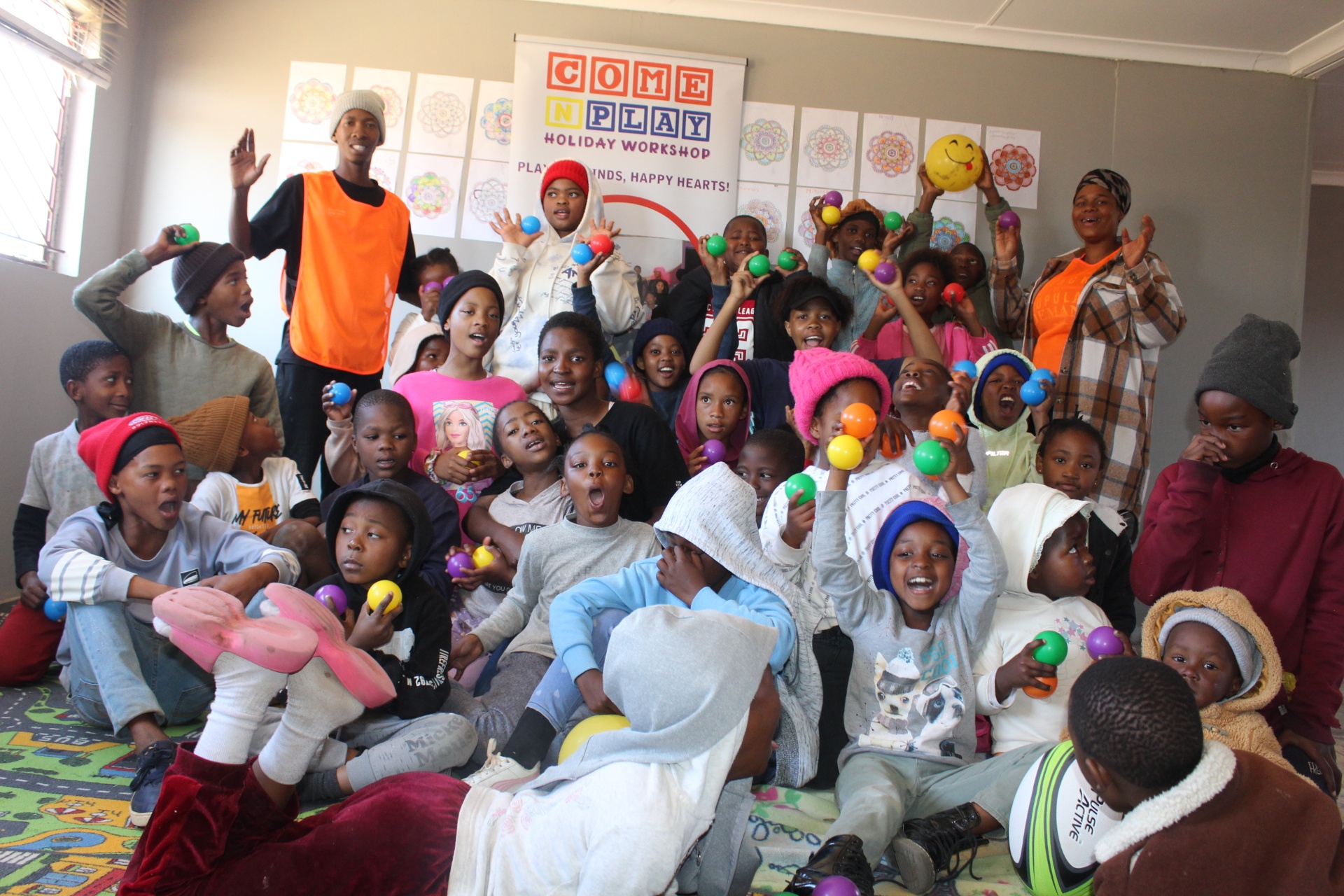 Cheerful children holding colourful balls in front of the Come N Play banner