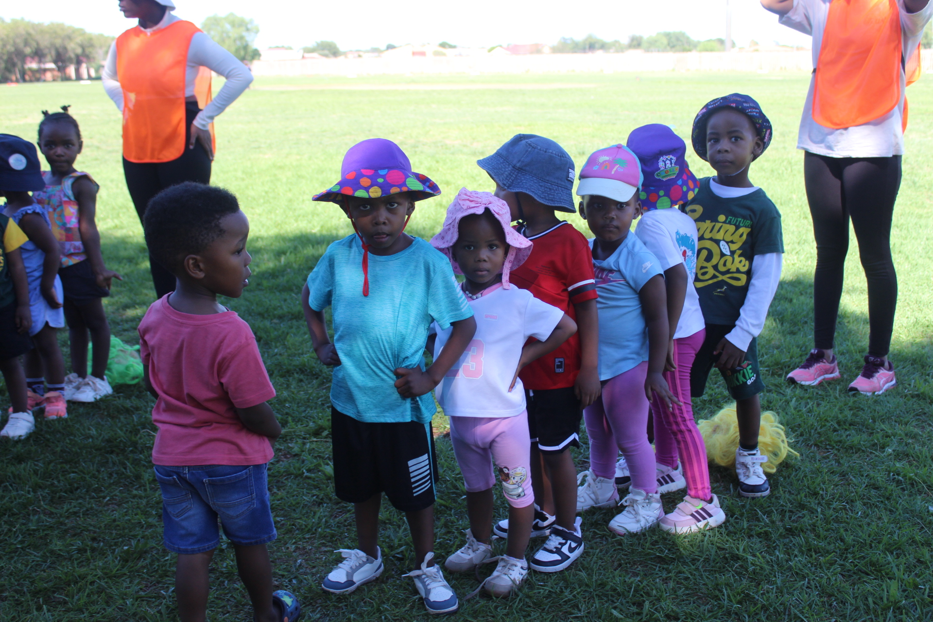 Young children in colourful sun hats lined up on the field for a Come N Play sports session