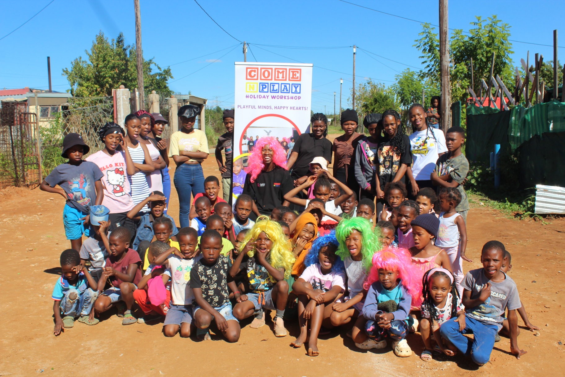 Group photo of children and facilitators with the Come N Play banner