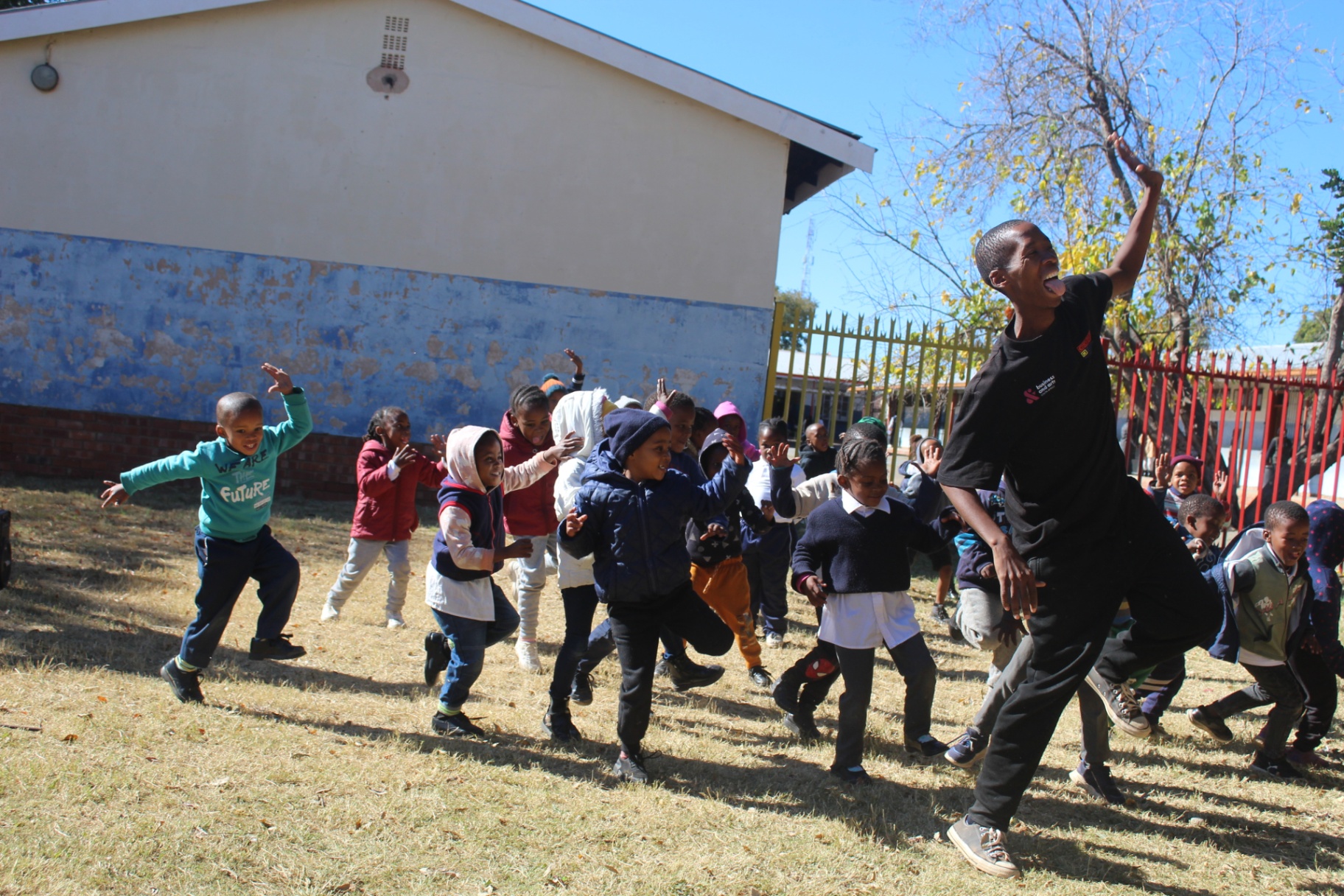 Children running joyfully across the schoolyard with a Come N Play facilitator during an outdoor session