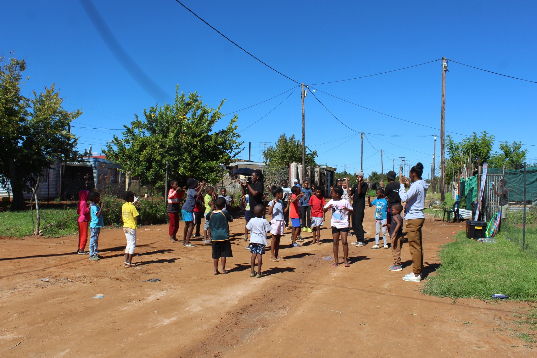 Facilitators leading a circle of children in a street-side dance and movement session in Kimberley